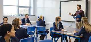 Teacher in front of a whiteboard delivering a lesson to a classroom of students.