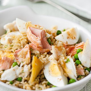 A bowl of cooked rice, boiled eggs, slices of fish and vegetables