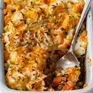 A mashed-potato-topped pie in a baking dish. A piece has been taken, showing chunks of butternut, tomatoes and vegetarian mince