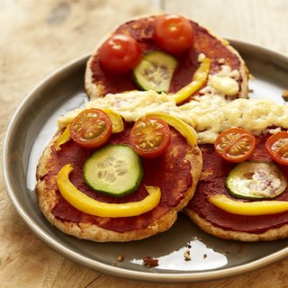 Smiley faces made from tomatoes, cucumber and peppers on pitta bread