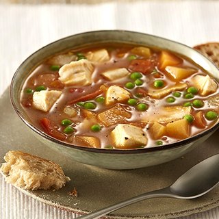 A bowl of brown broth, with chunks of chicken, carrots and peas visible.