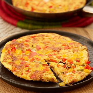 A plate with a golden omelette that has different-coloured chunks of pepper