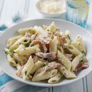 A serving of penne carbonara, with chopped parsley and bacon