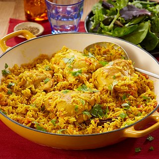 A large pot of spiced rice, chicken, carrot and tomatoes, served with a green salad.