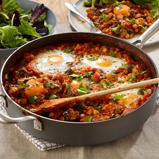 A pan filled with a tomato sauce comprising aubergine, chickpeas and poached eggs, served with pitta.