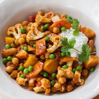 Vegetable jalfrezi curry, with peas, chickpeas and peppers, served in a bowl with a spoonful of yoghurt