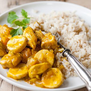 Slices of curried chicken and banana, served on a plate with rice