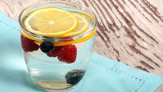 A glass of water with slices of orange, raspberries and blueberries added