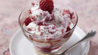 The image shows two glass dessert cups filled with creamy Greek yogurt and garnished with fresh raspberries. The yogurt appears to be mixed with raspberries, giving it a pinkish colour with visible fruit chunks. The dessert looks refreshing and is attractively presented.