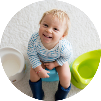 Toddler sits on a potty and smiles at the camera.