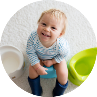 Toddler sits on a potty and smiles at the camera.