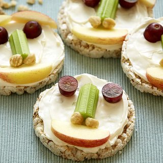 A rice cake with a fun face, assembled from grapes, celery, nuts and apple