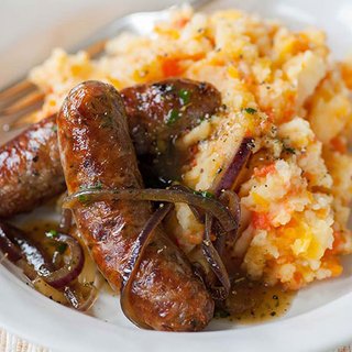 Grilled sausages served with mashed potato covered in gravy.