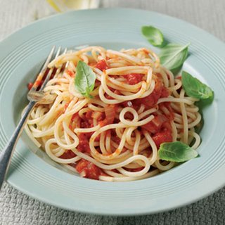 A plate of spahetti with tomato sauced, topped with basil leaves