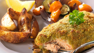 Salmon, cooked in pesto and parmesan, served on a plate with mixed vegetables.