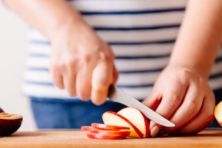A person cutting half an apple into thin slices