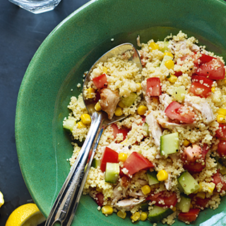 A serving of couscous topped with chicken, tomato and cucumber