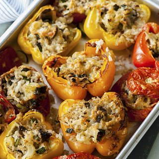 A tray of baked tomatoes and peppers, stuffed with a rice mixture and topped with melted cheese.