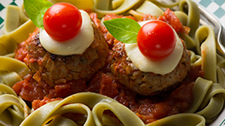 2 meatballs with tomatoes as eyes, on a bed of pasta.