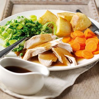 A Sunday roast dinner, with chicken, potatoes, carrots, cabbage and gravy