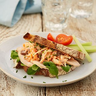 A turkey and coleslaw sandwich, with accompanying tomatoes and celery