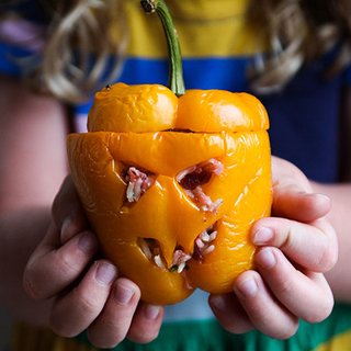 A yellow pepper with a scary face carved into it, stuffed with beetroot-red rice