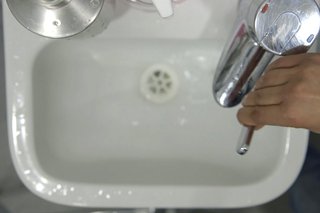 Hand turning the tap on in a sink