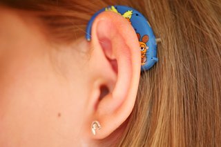 A close-up image of a young person's left ear with a blue hearing aid behind their ear.
