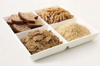 Four bowls containing different types of starchy foods: wholewheat pasta, wholemeal bread, brown rice and bran flakes