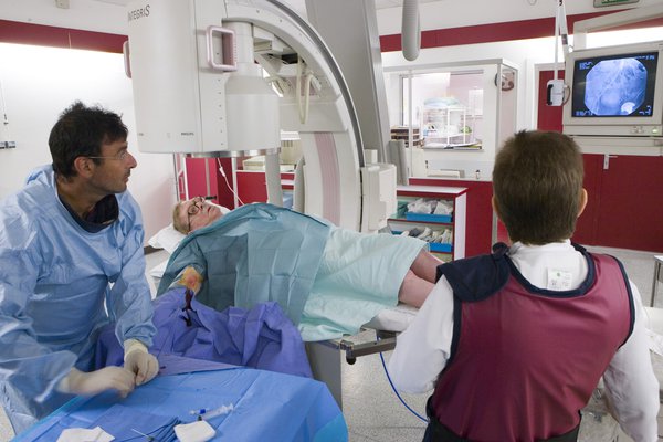 A patient lying on an X-ray table next to a doctor looking at an image of the patient's blood vessels on a screen