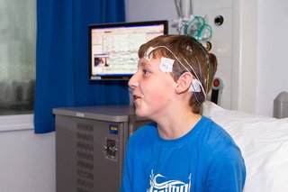 A young boy in hospital with coloured wires and electrodes attached to his head with tape.