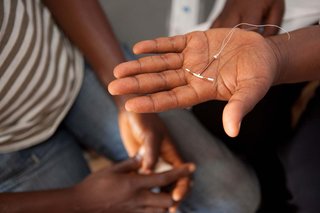 Someone holding an IUD (intrauterine device). It is a thin plastic t-shape about a quarter of the size of their palm.