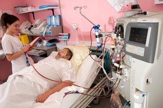 A man lying on a hospital bed connected to a large haemodialysis machine by a number of tubes.