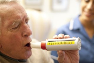 A man blowing into a small tube (peak flow meter). There’s a number scale on the side to measure how fast he can breathe out.