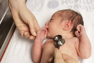 Close-up of a person's hand holding a stethoscope to a newborn baby's chest.