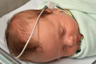 Close-up of a baby's head with an earpiece attached to a wire in their left ear.