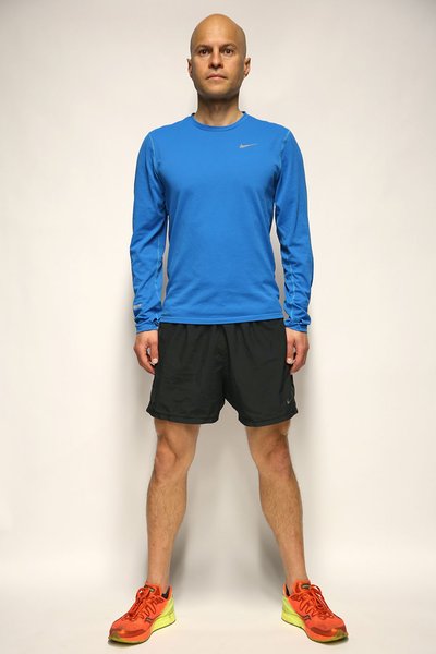 A man standing in the wall squats starting position, with his back against a wall and feet hip-width apart.