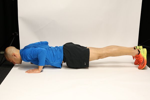 Man lying face down propped up on hands and toes, with legs straight and elbows bent. His body forms a straight line and he is very close to the floor.