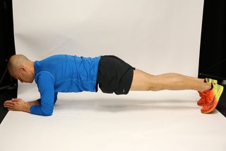 Man lying face down, propped up on forearms and toes, with legs straight and hips raised to create a straight line from head to toe.