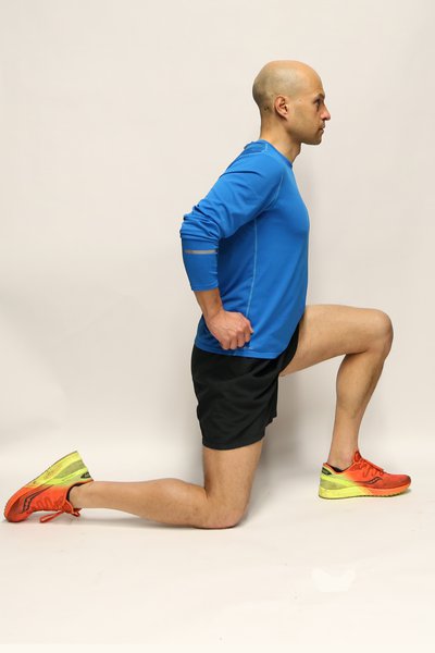 Man kneeling down on his right knee, leaning forwards. He is looking straight ahead and his hands are on his hips.