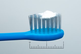 a child's blue toothbrush with a pea-sized amount of toothpaste on it next to a 2cm scale