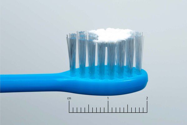 A child's blue toothbrush with a smear of toothpaste on it next to a 2cm scale.