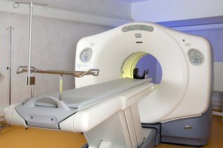 A PET scanner machine with a short tunnel through the middle, and a narrow, flat bed attached that can move through the tunnel.