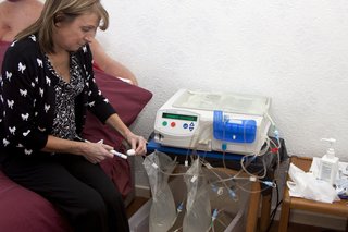 A woman preparing to have dialysis at home. She’s attaching herself to a dialysis machine that is sitting on a bedside table.