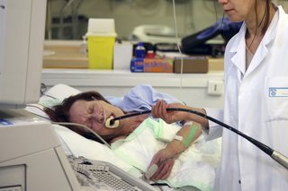Person lying on their side with a black tube in their mouth, which is being held by a radiographer as they look at a screen.