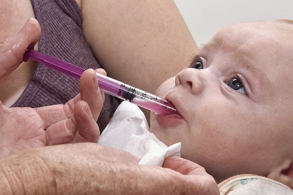 An image of a person putting a syringe of medicine into a baby's mouth.