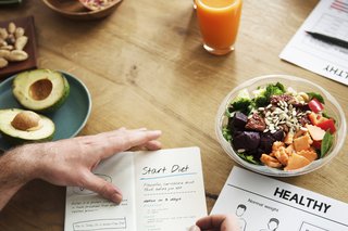 A table with a bowl of salad and a person writing a diet plan