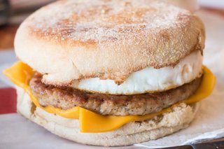 A fried egg, beef burger and a slice of processed cheese in between two halves of an English muffin.