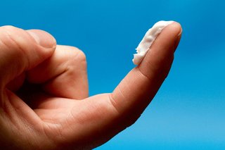 A strip of cream on an adult's finger. The cream goes from the fingertip down to the first joint of the finger.