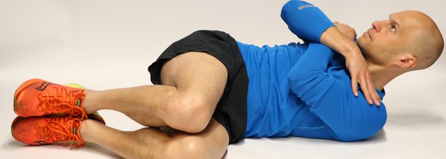 Man lying on back, knees bent and rolled to one side to the floor. Hands are crossed over the chest.